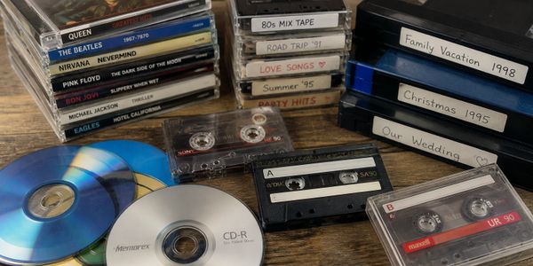 A collection of vintage music CDs, cassette tapes, and VHS tapes with handwritten labels.