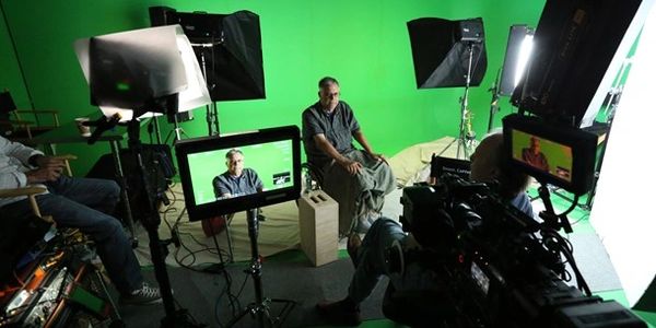 A man being interviewed on a green screen set with multiple cameras and lights around.