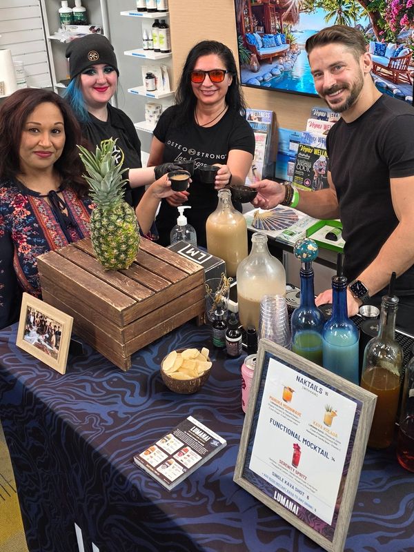 Four people smiling behind a LUMANAI display table with drinks and pineapple.