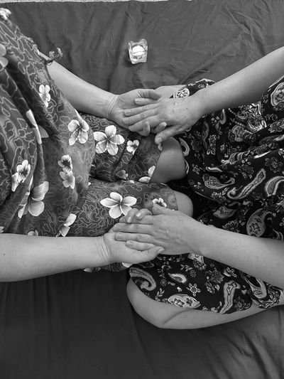 Two people holding hands, sitting close together on a bed.