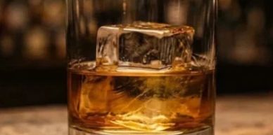 Glass of whiskey with ice cube.