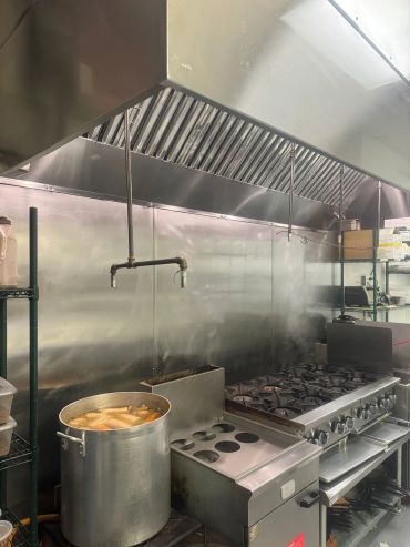 Commercial kitchen stove with a large pot simmering and stainless steel surroundings.
