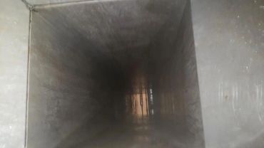 Inside view of a long, empty rectangular duct or tunnel with faint light at the far end.