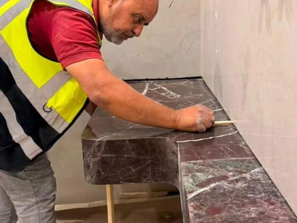 Worker measuring marble countertop edge.