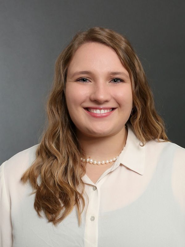 Smiling woman with wavy hair in white shirt and pearl necklace.