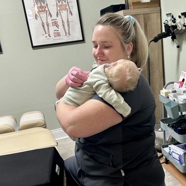 Healthcare worker hugging a baby in a medical office.