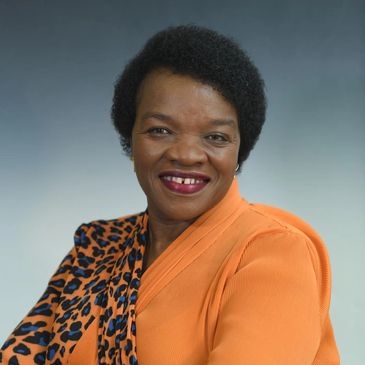 Smiling woman in orange and leopard print attire against a gray background.