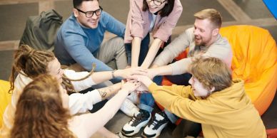 A diverse group of friends team up with hands together in a circle indoors.