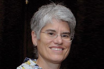 Smiling person with short gray hair and glasses.
