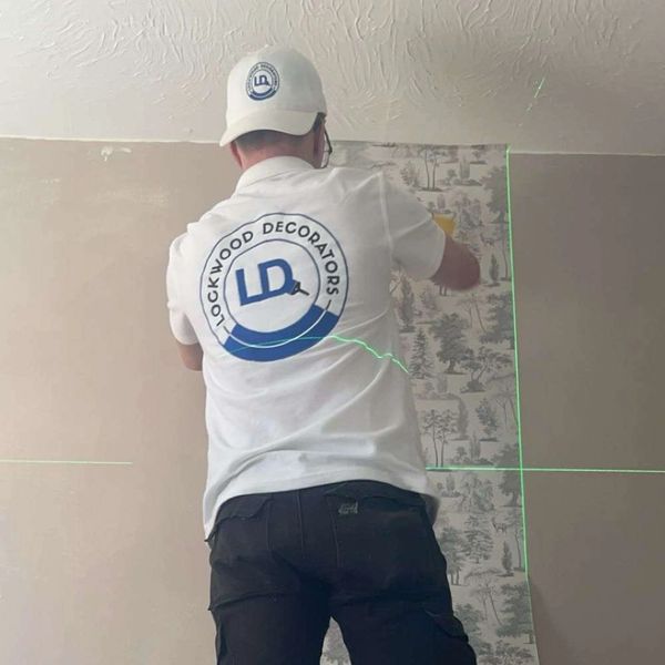 A decorator installing wallpaper using a laser level for precision.