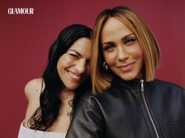 Two smiling women posing closely against a red background for Glamour.