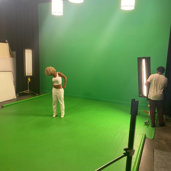 Person posing in a green screen studio with lighting setup.