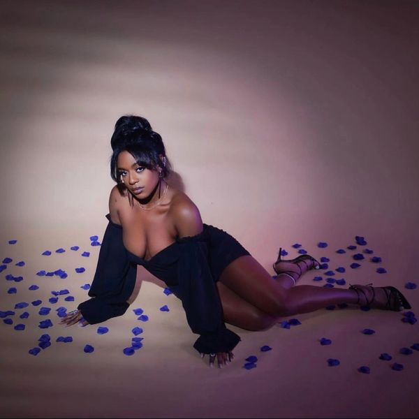 Woman in black dress poses on floor with blue petals scattered around her.