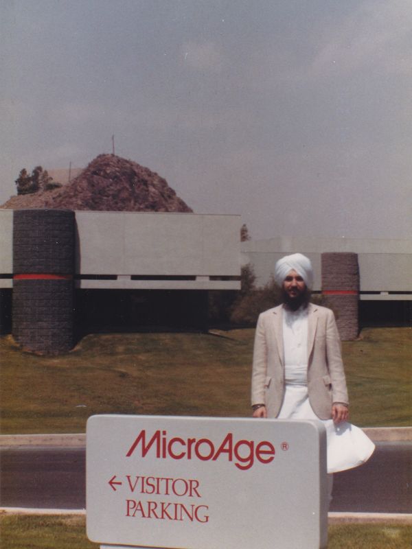 Man in turban standing by MicroAge visitor parking sign.