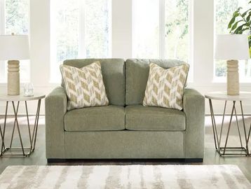 Green loveseat with patterned cushions flanked by side tables and lamps.