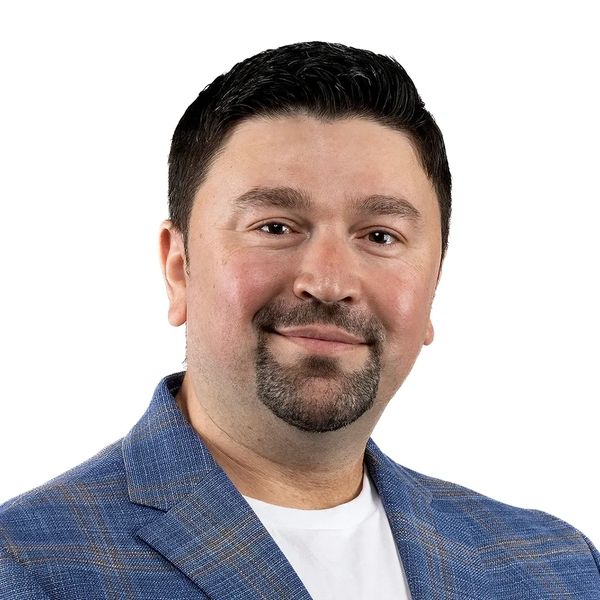 Smiling man in a blue blazer with a white shirt on a white background.