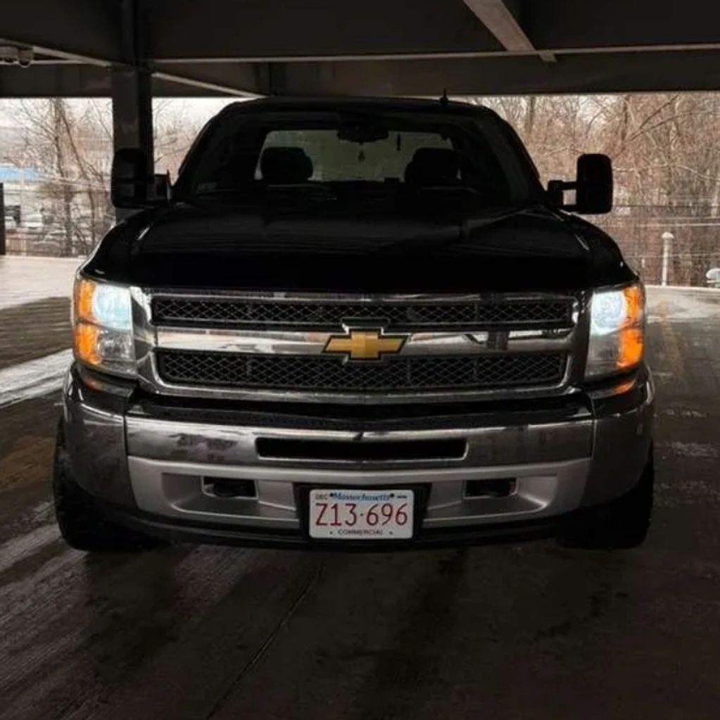 Front view of a black Chevrolet truck with headlights on in a shaded area.