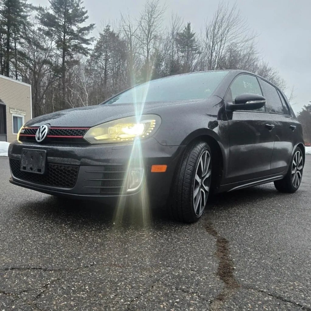 Black Volkswagen hatchback with headlights on in overcast weather.