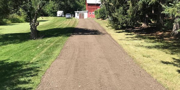 A gravel driveway on a farm leading to a red barn.