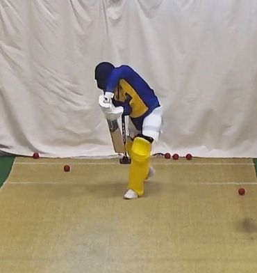 Cricket player practicing batting indoors with protective gear.