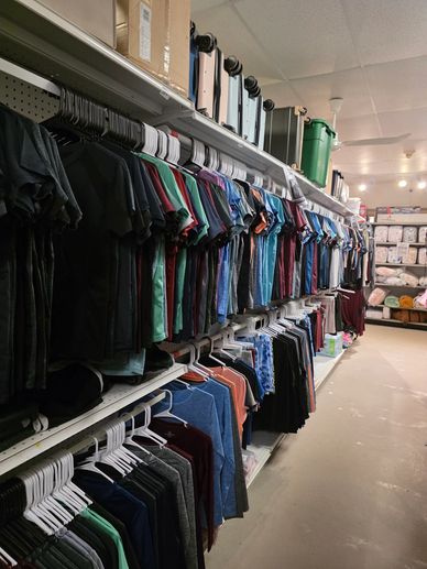 Clothing store aisle with shirts and luggage on shelves.