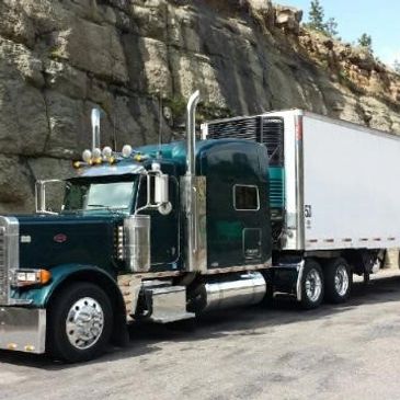 A large green semi-truck with a white trailer parked by a rocky cliff.