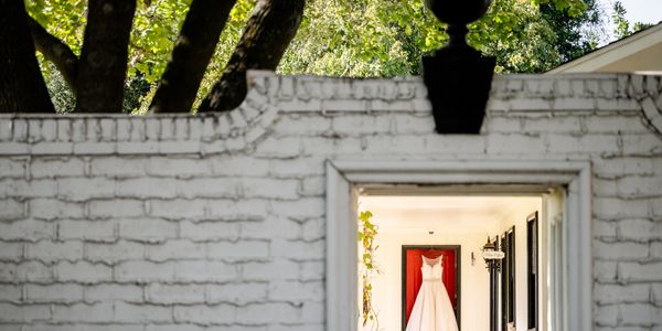 White wedding dress hanging indoors seen through an opening in a white brick wall.