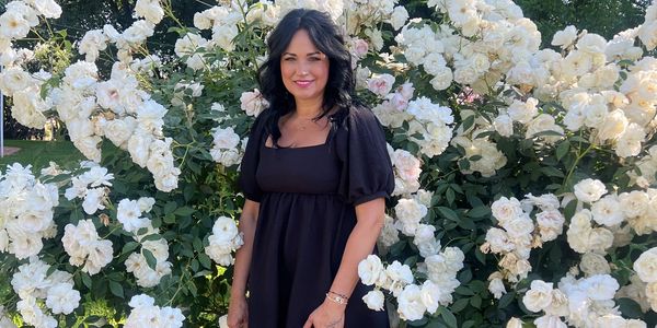 Woman in black dress standing by white roses.