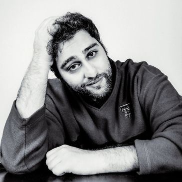 A black and white portrait of a man with a gentle smile, resting his head on his hand.