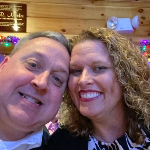 Smiling couple taking a close-up selfie in a warmly lit indoor setting.