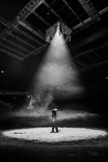 A person stands alone under a dramatic spotlight in a dark, foggy room.