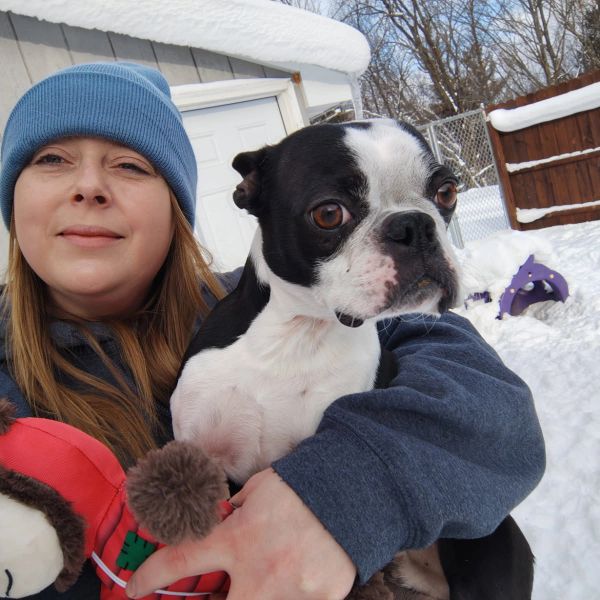 Woman in blue hat holding a black and white dog in snowy backyard.