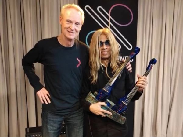 Two men posing, one holding a unique double-necked guitar.
