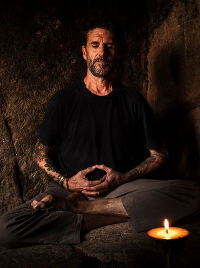 Man meditating cross-legged by candlelight in a dim setting.
