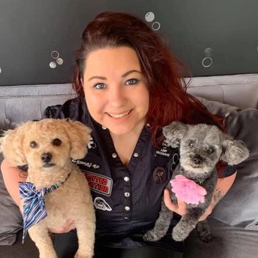 Woman smiling with two small dogs wearing accessories on a couch.