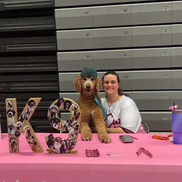 Person sitting with a poodle at a decorated table with dog photos.
