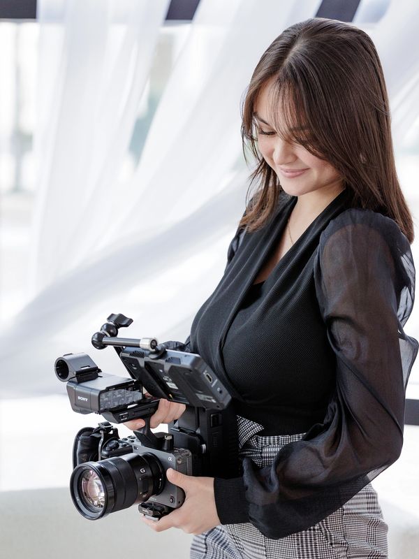 Woman holding a professional video camera and smiling.