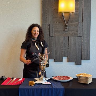 Woman serving cured meat at a table with a slicer.