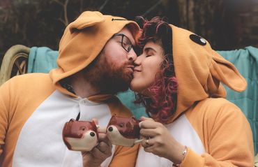 Couple in matching animal onesies sharing a tender kiss while holding cute animal mugs.