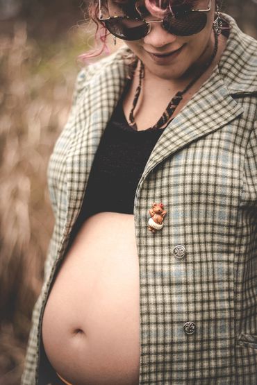Pregnant woman wearing sunglasses and a checkered jacket, smiling down at her belly.