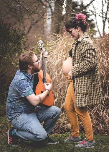Man playing guitar for pregnant woman in autumnal outdoor setting.