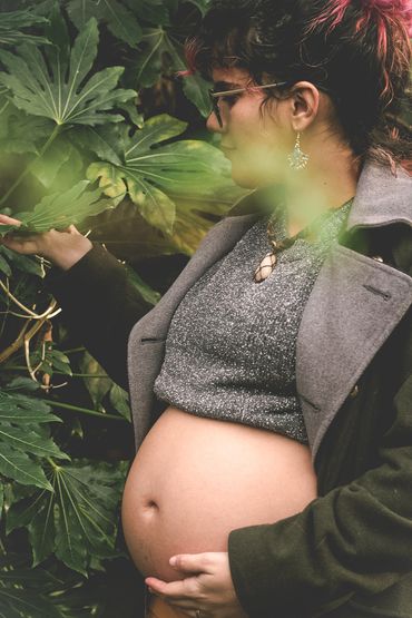 Pregnant woman gently touching leaves, surrounded by greenery.