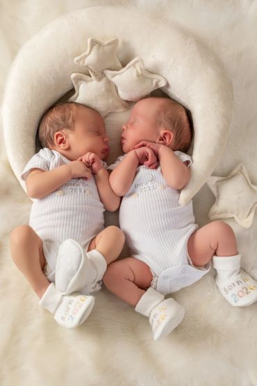 Newborn twins sleeping peacefully on a soft, star-themed cushion.