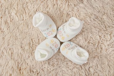 Four baby socks arranged in a circle on a soft beige carpet.