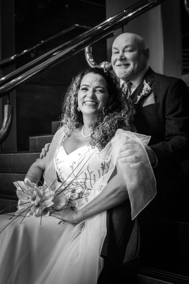 Smiling bride and groom pose on stairs in a joyful wedding portrait.