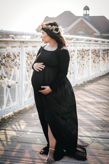 Pregnant woman in black dress standing on a bridge adorned with locks.