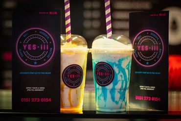 Two colorful milkshakes with striped straws and promotional signs for 'YES-III' drinks.