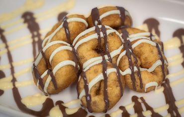 Fried doughnuts drizzled with white and dark chocolate on a white plate.