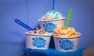 Three colorful ice cream cups held by a gloved hand.