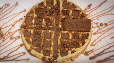 A waffle topped with chocolate sauce, crumbled cookies, and a whole cookie on the side.